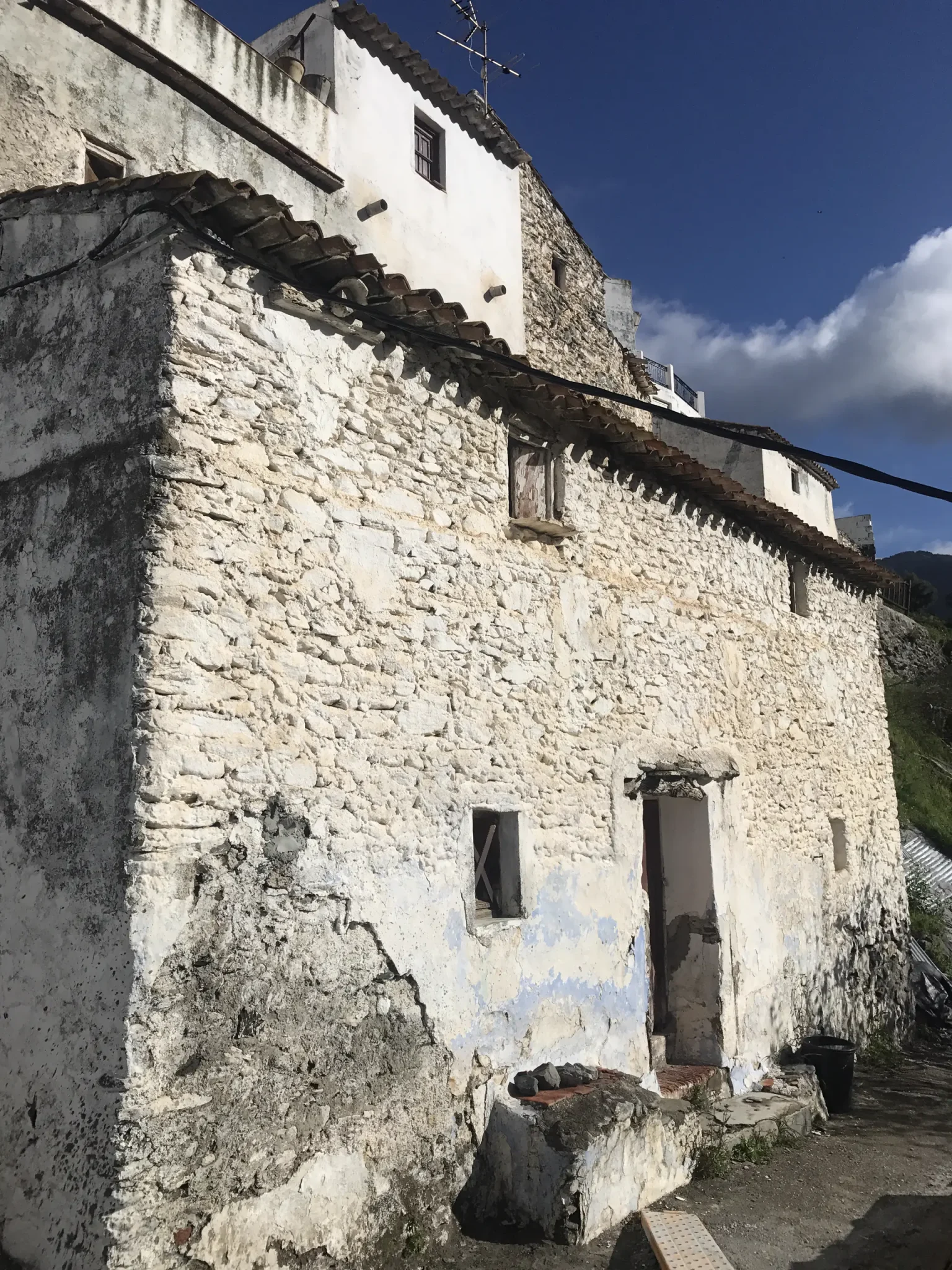 Fachada de una casa tradicional de piedra con restos de cal, tejado de teja árabe y entrada con escalón de piedra